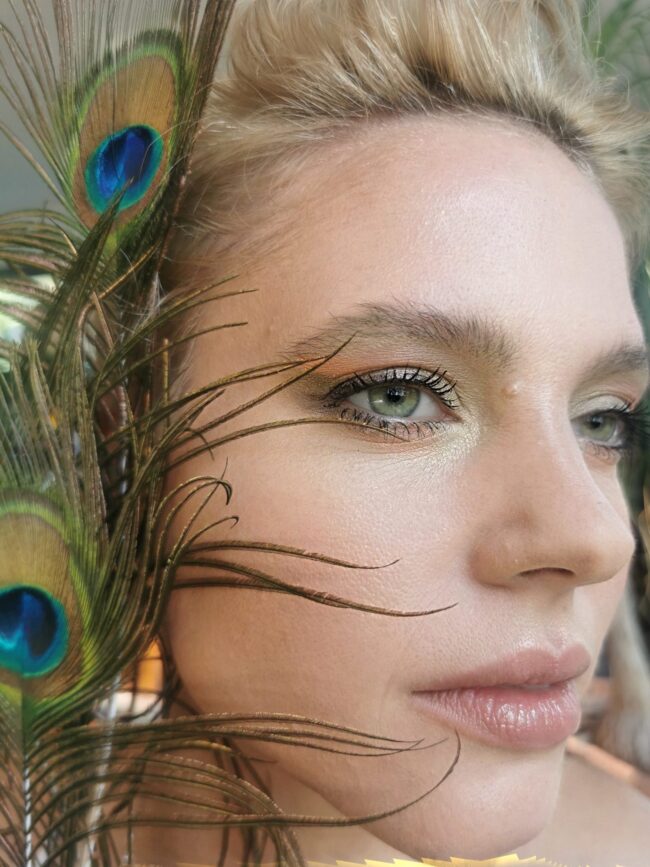Beauty portrait with a peacock feather, glowing skin and soft green eyeshadow — make-up by Blandine Lagoutte